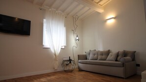 A living room with a sofa, a flat-screen TV, a table with a lamp, and a window with curtains. - Tornabuoni Loft Apartment (Firenze)