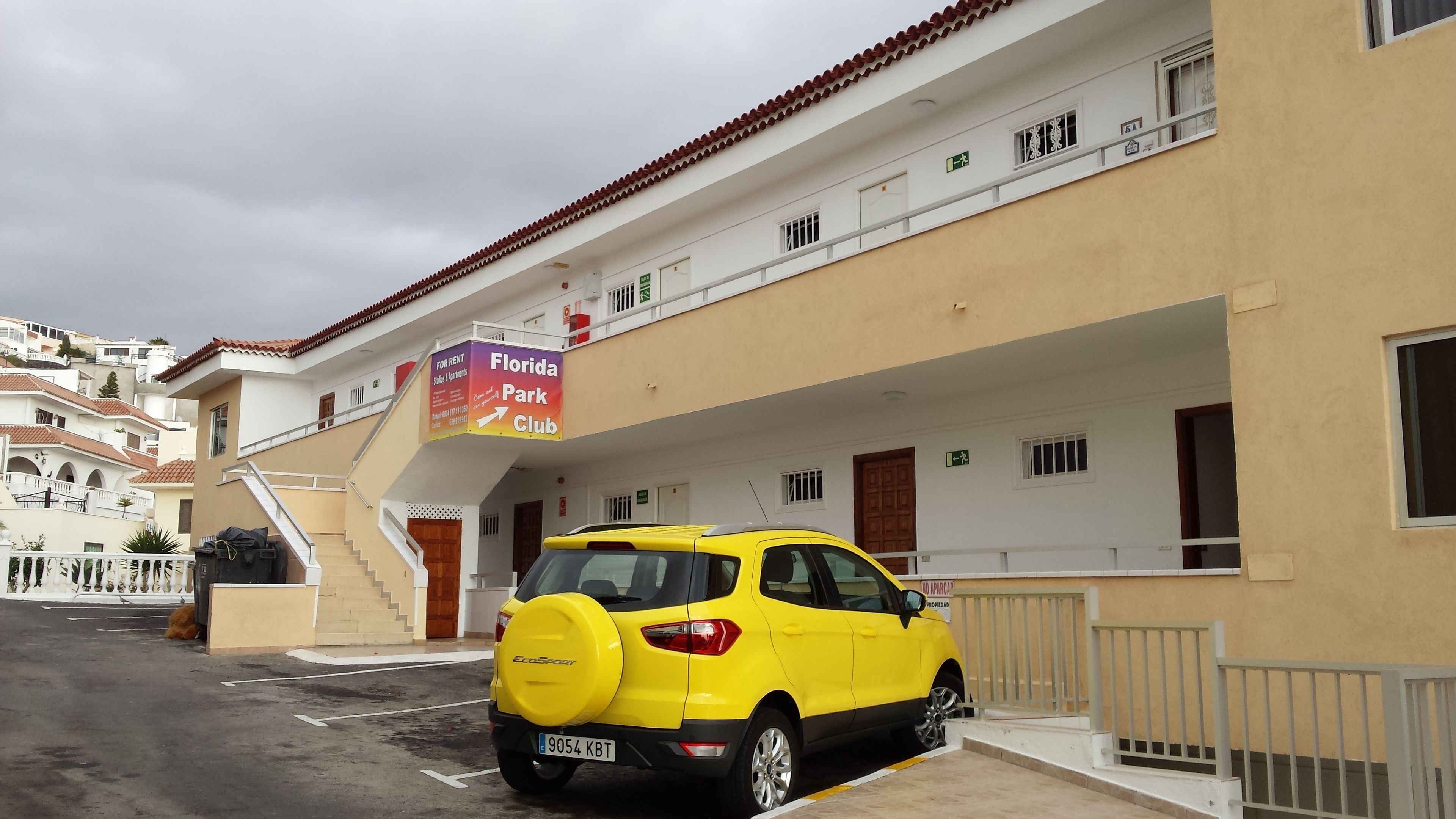 A yellow car parked in front of a building with a sign for a Florida Park Club.