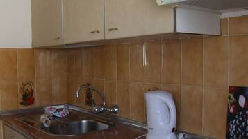 Una cocina con armarios color beige, un lavamanos de acero inoxidable, una tetera blanca y una estufa integrada.