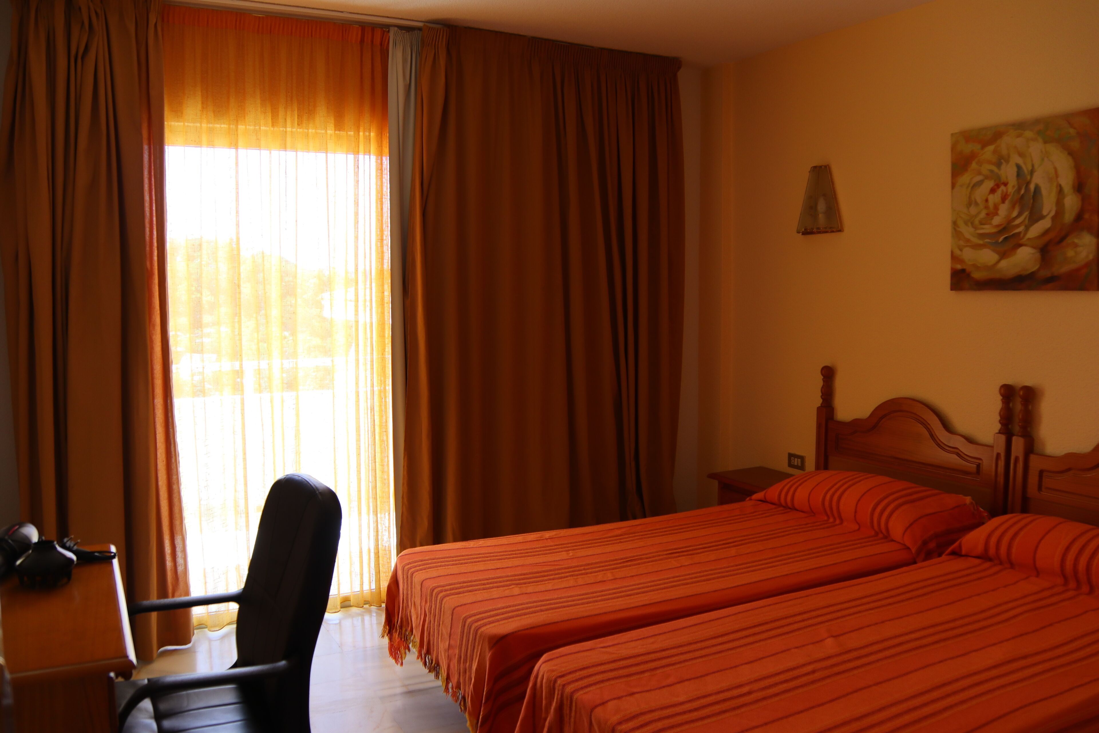 A hotel room with two beds, a chair, a desk, and a painting on the wall.