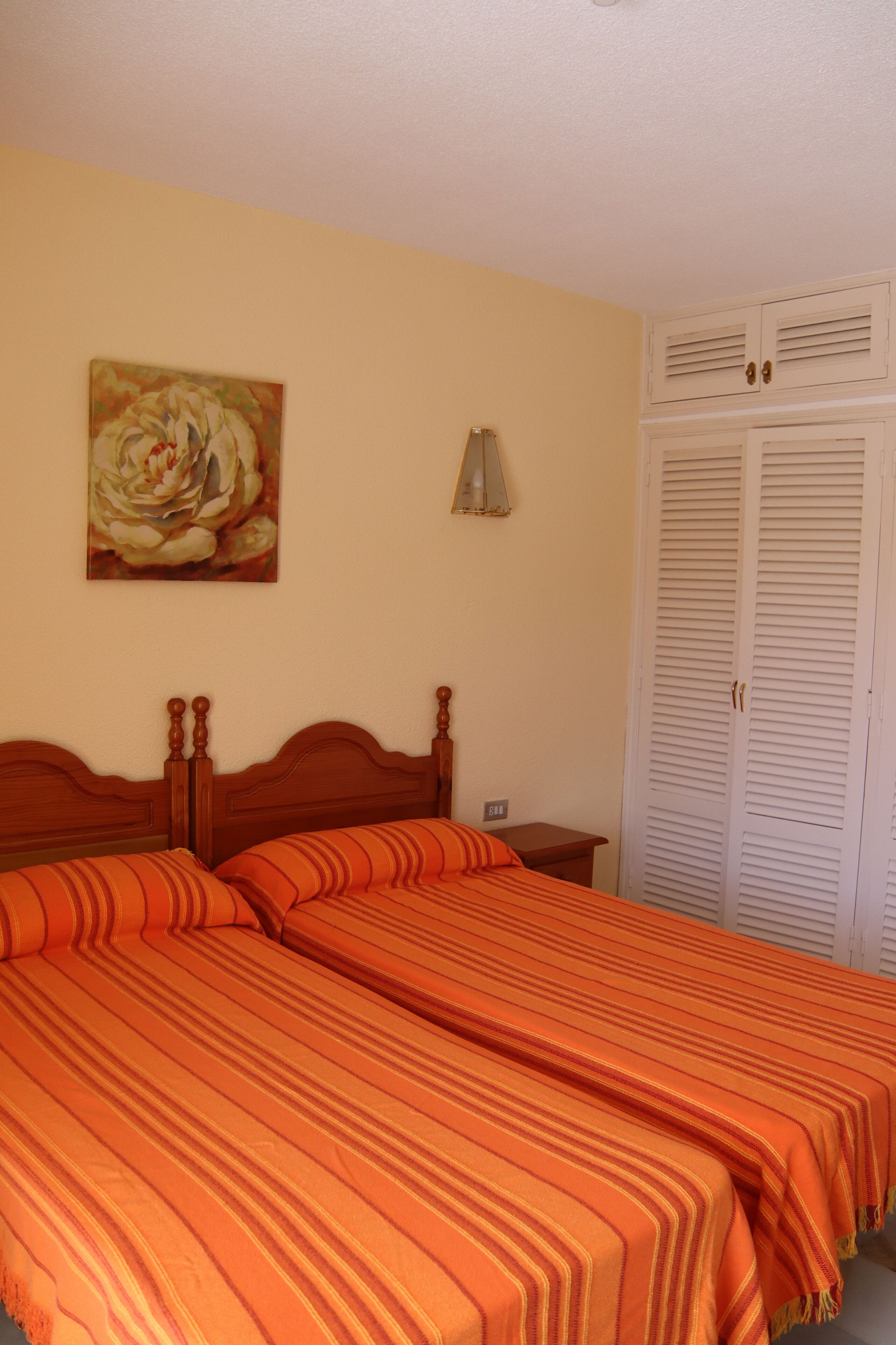 A bedroom with two beds, a painting on the wall, a nightstand, and a closet.