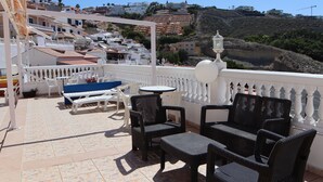 Une terrasse dotée de meubles en osier, d’une table de billard et offrant une vue sur une colline parsemée de bâtiments.