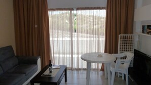 Un salon comprenant un canapé, une table basse, une table à manger avec des chaises, et une vue à travers une porte vitrée.