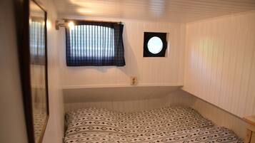 A bedroom with a bed, a window with blinds, a small circular window, and a mirror.