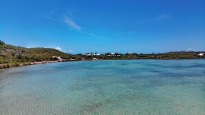 Un paisaje costero con aguas turquesas cristalinas, un telón de fondo montañoso y un conjunto de edificios con techos blancos.