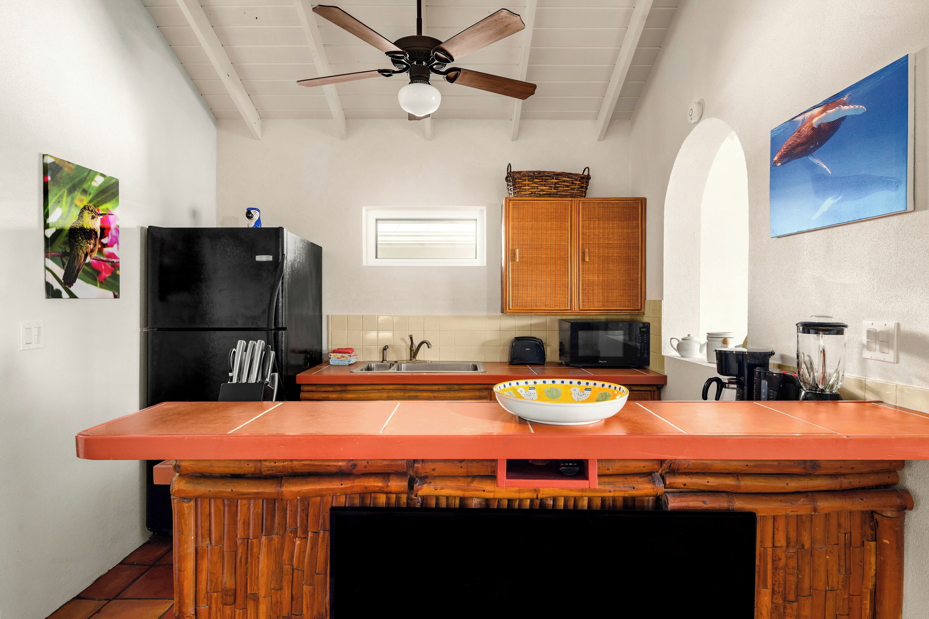 Une cuisine avec un îlot central en bois, un réfrigérateur noir, un four à micro-ondes et un ventilateur de plafond.