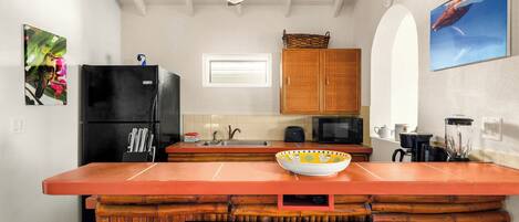 Une cuisine avec un îlot central en bois, un réfrigérateur noir, un four à micro-ondes et un ventilateur de plafond.