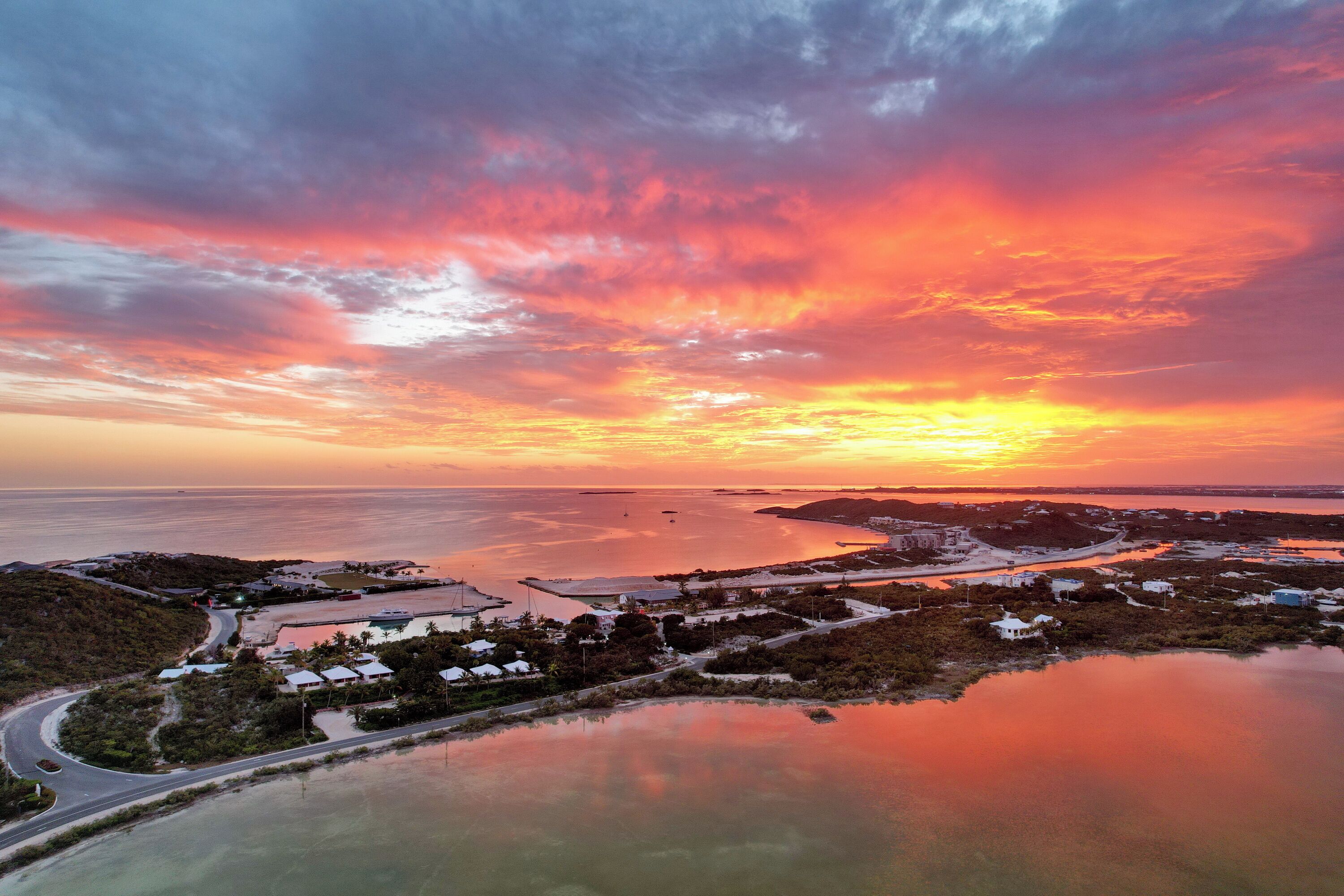Et kystlandskab med solnedgang over vandet, veje og spredte bygninger.