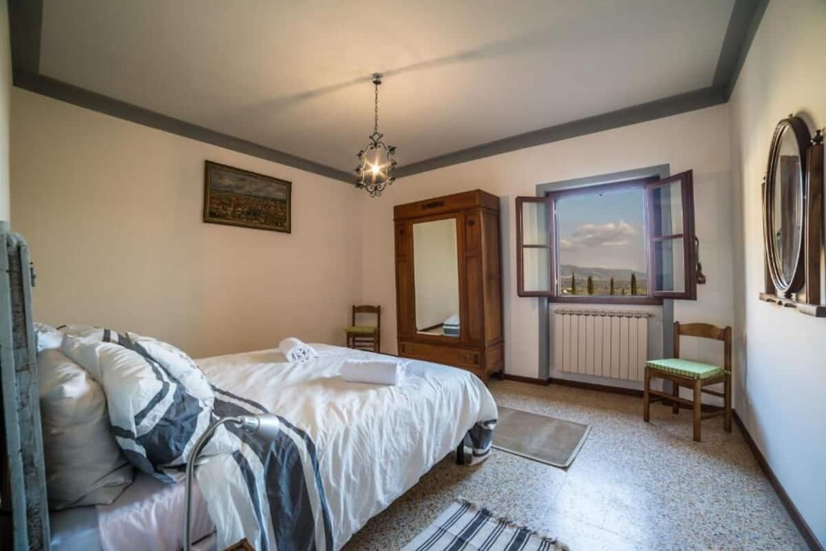 Une chambre à coucher avec un lit, une fenêtre donnant sur un paysage agréable, un miroir et un radiateur.