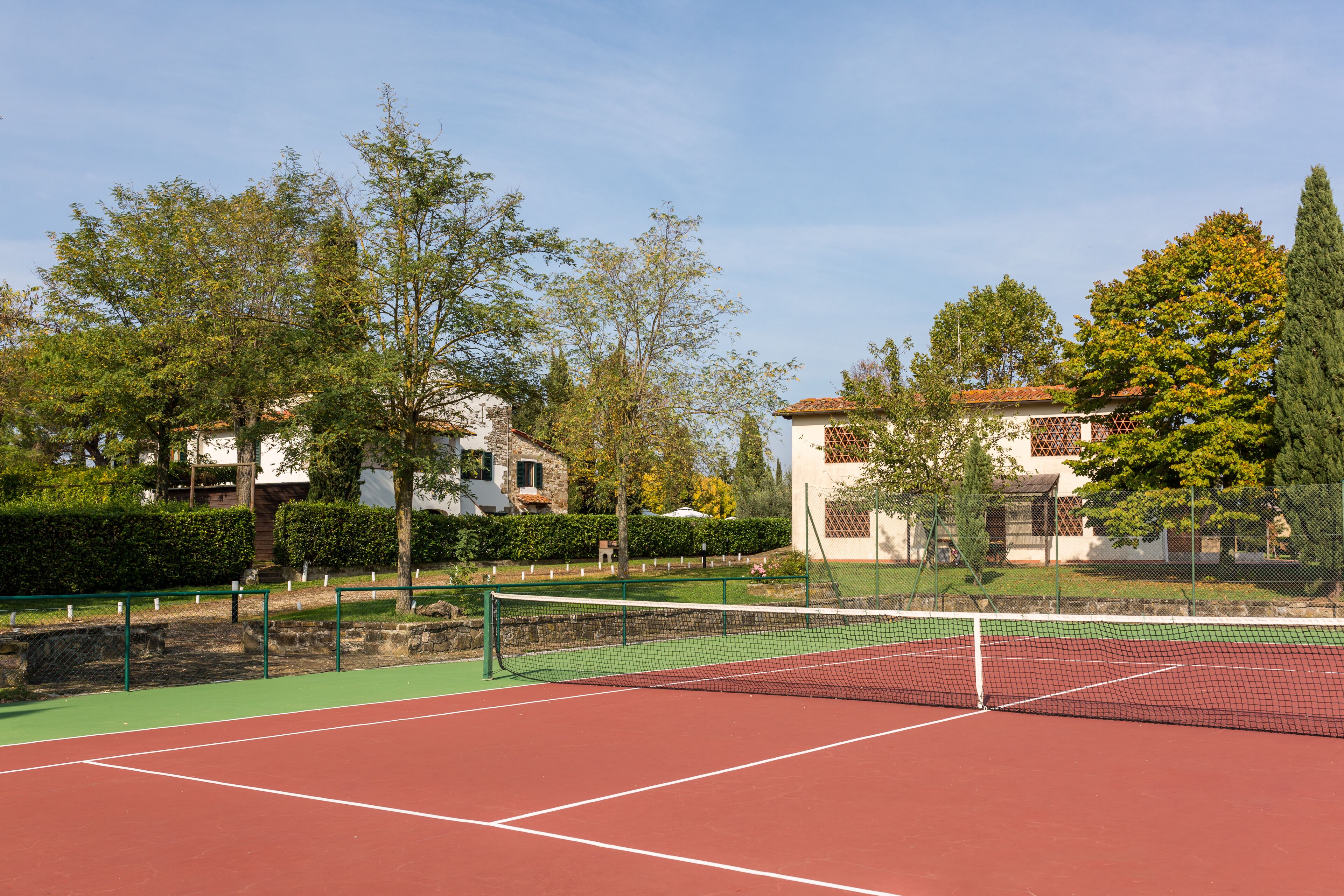 A tennis court with a net, surrounded by trees and buildings.