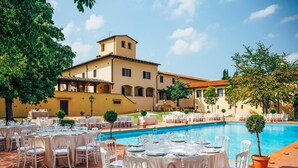 Un espace extérieur avec une piscine, des tables et des chaises rondes, un bâtiment doté d’un toit en tuiles et un ciel dégagé.