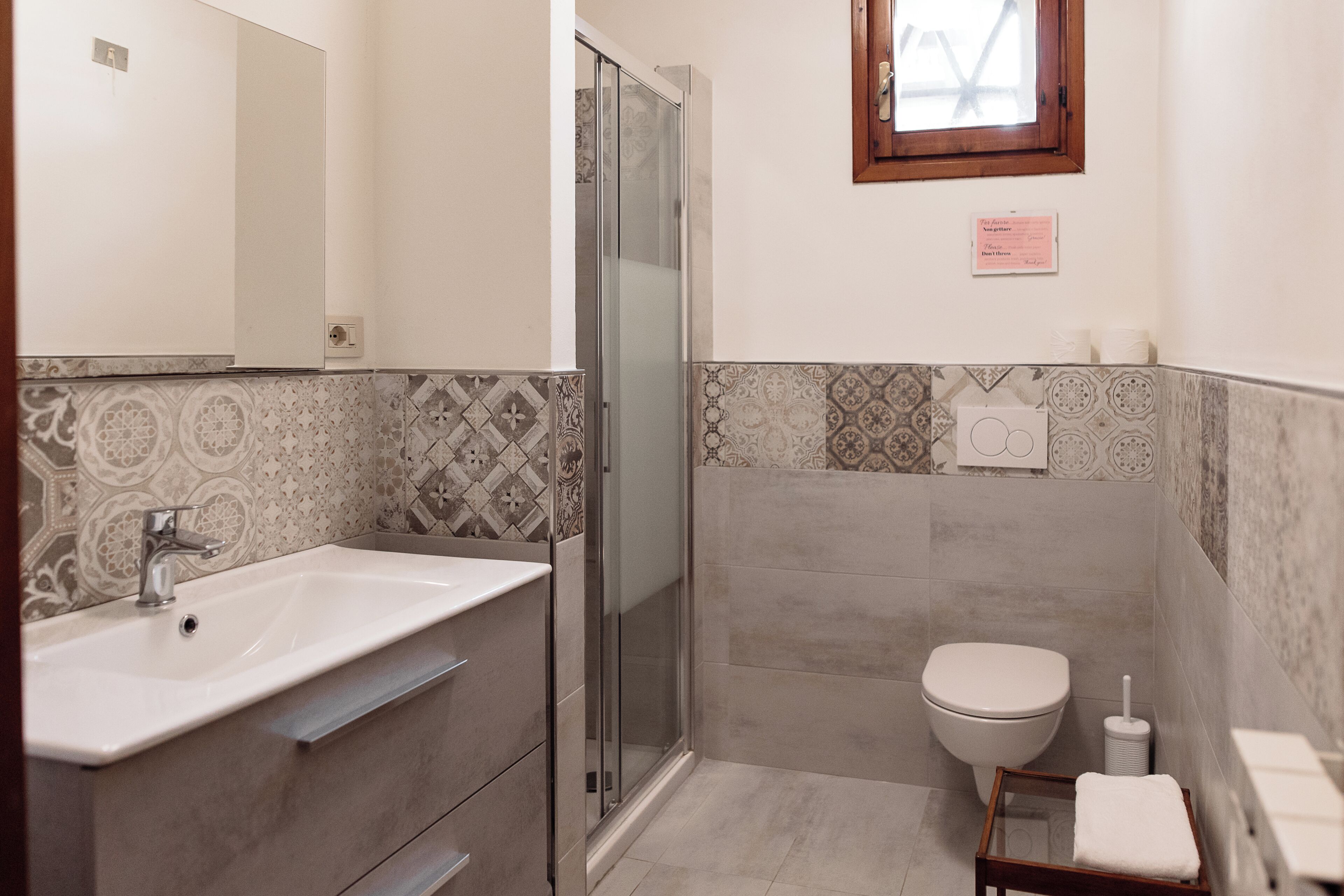 Casa de banho com lavatório, espelho, sanita e cabine de duche em vidro.