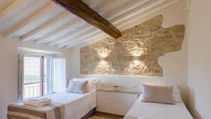 Une chambre avec deux lits, un mur en pierre et une fenêtre.