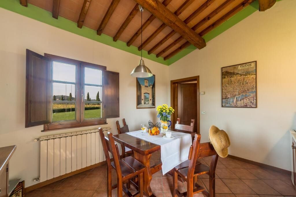 Un comedor con una mesa preparada para cuatro personas, sillas de madera, una lámpara colgante y vistas a través de una ventana.