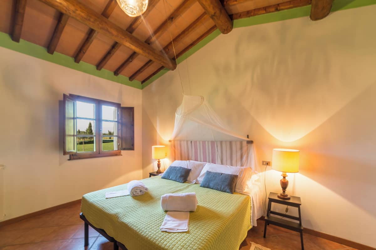 Une chambre à coucher avec un lit, des lampes de chevet, une fenêtre avec des rideaux et un plafond en bois.
