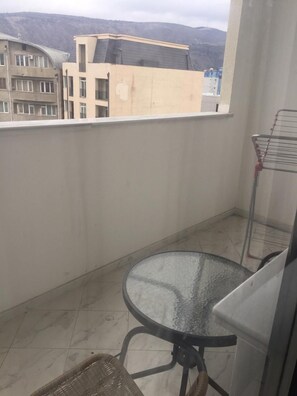A balcony with a glass table and wicker chair, a metal rack, and a view of buildings and hills. - Apartment on Berbuki str. (Tbilisi)