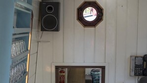 A narrow hallway with a wooden door, a speaker mounted on the wall, and a telephone.