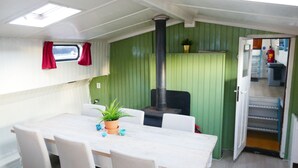 A compact kitchen with a central stove, a dining area with a table and chairs, and a small window with red curtains.