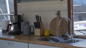 A kitchen with a sink, a coffee maker, a kettle, a knife block, and a wooden cutting board.