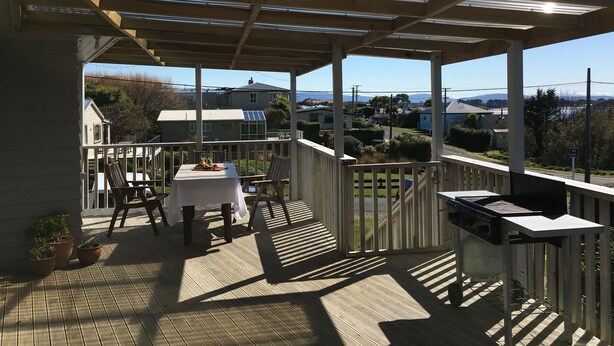 A covered outdoor area with a table and chairs, a grill, and a view of houses and mountains. - Rob's Beach House Riverton (Riverton)