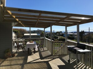 A covered outdoor area with a table and chairs, a grill, and a view of houses and mountains.
