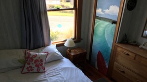 A bedroom with a bed, a nightstand, a dresser, a window with a view of a beach, and a lamp. - Rob's Beach House Riverton (Riverton)
