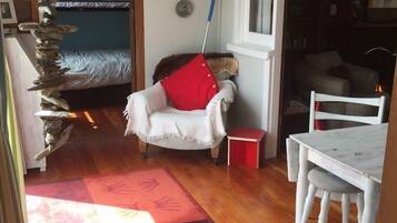 A cozy room with a bed, a chair with a red pillow, a small table, and a unique wall decoration.