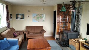 Una sala de estar con un sofá marrón, un sofá azul, una mesa de centro de madera, un mapa en la pared, una chimenea con chimenea y un televisor sobre un mueble de madera.