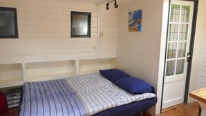 A bedroom with a bed, a window, a door, and a small wall-mounted shelf. - Boat apartment Rotterdam Fokkelina (Rotterdam)