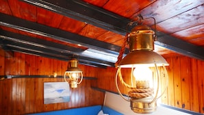 A wooden interior with a blue sofa, a wooden table, and two hanging lanterns. - Boat apartment Rotterdam Fokkelina (Rotterdam)