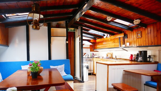 A cozy kitchen with wooden cabinets, a central island, and a blue sofa. - Boat apartment Rotterdam Fokkelina (Rotterdam)