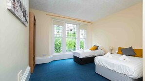 A bedroom with two beds, a large window with a view, and a blue carpet. - The New Mill Apartments (Newcastle-upon-Tyne)