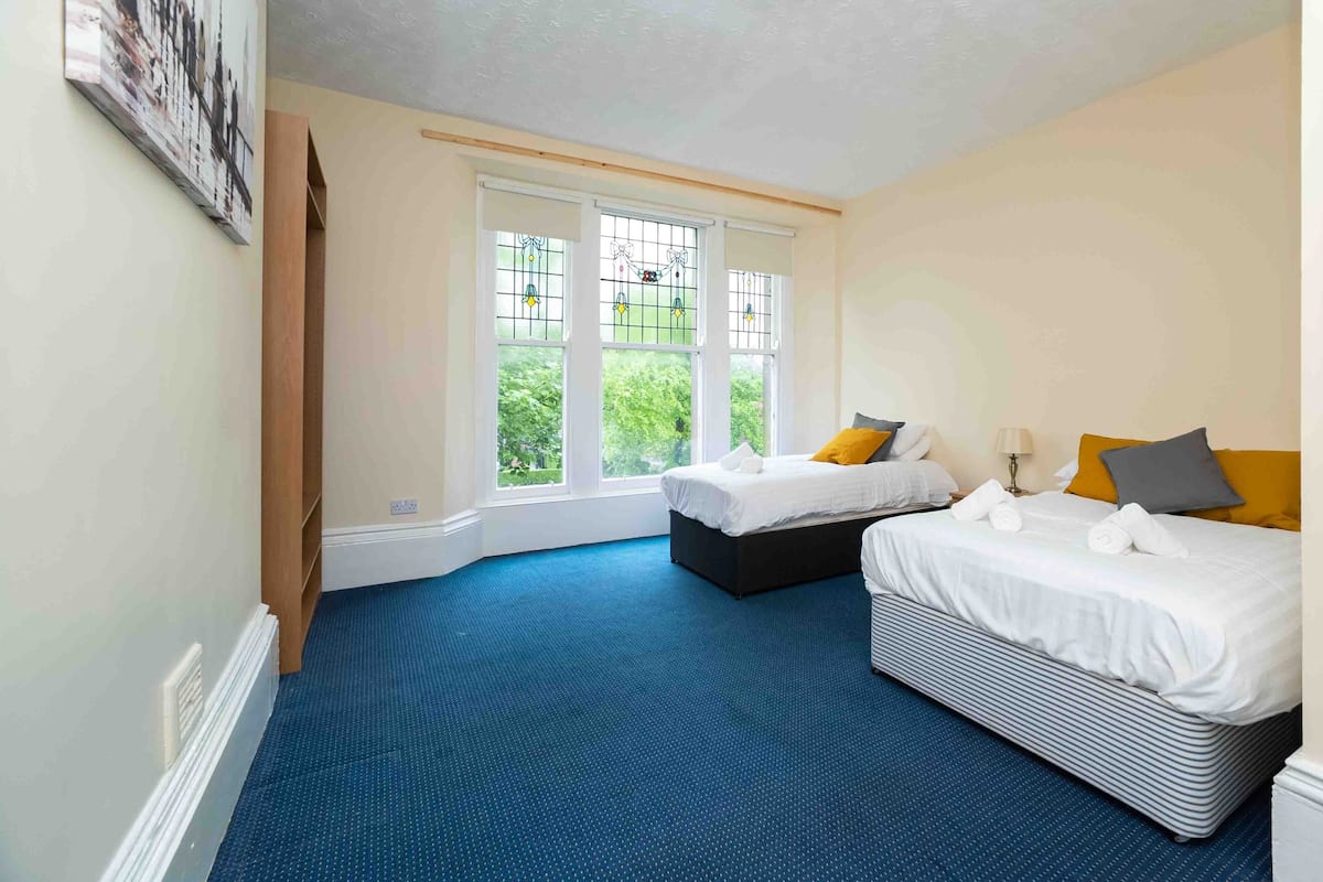 A bedroom with two beds, a large window with a view, and a blue carpet.