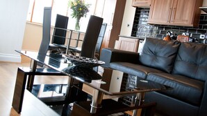 A modern living room with a glass dining table, black leather sofa, and wooden cabinets. - The New Mill Apartments (Newcastle-upon-Tyne)
