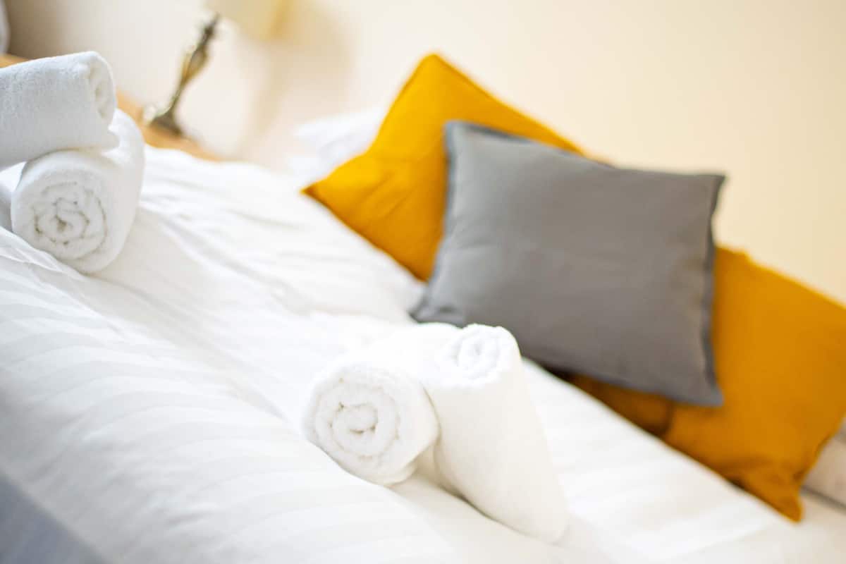 A neatly made bed with rolled white towels and two pillows, one yellow and one gray.