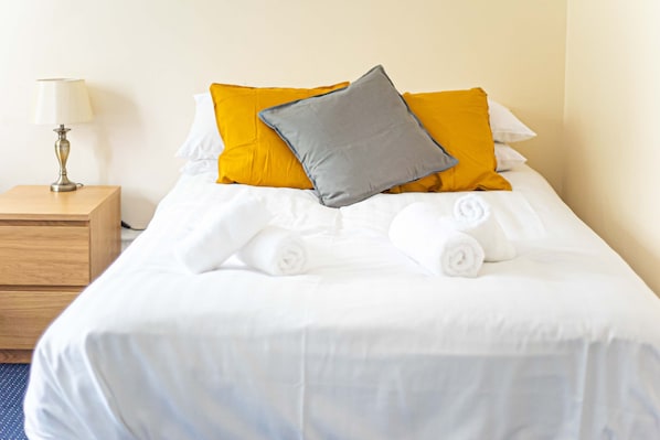 A neatly made bed with white linens, two rolled towels, and two pillows (one yellow and one gray). - The New Mill Apartments (Newcastle-upon-Tyne)