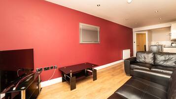 A living room with a red wall, a black leather sofa, a wooden coffee table, and a flat-screen TV.