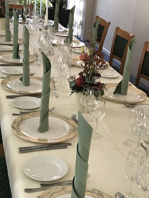 A long dining table set with plates, cutlery, and wine glasses, with green napkins and a floral centerpiece.