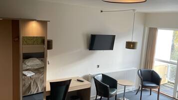 Una habitación de hotel compacta con una cama, un escritorio con una silla, un televisor y una ventana con vistas.