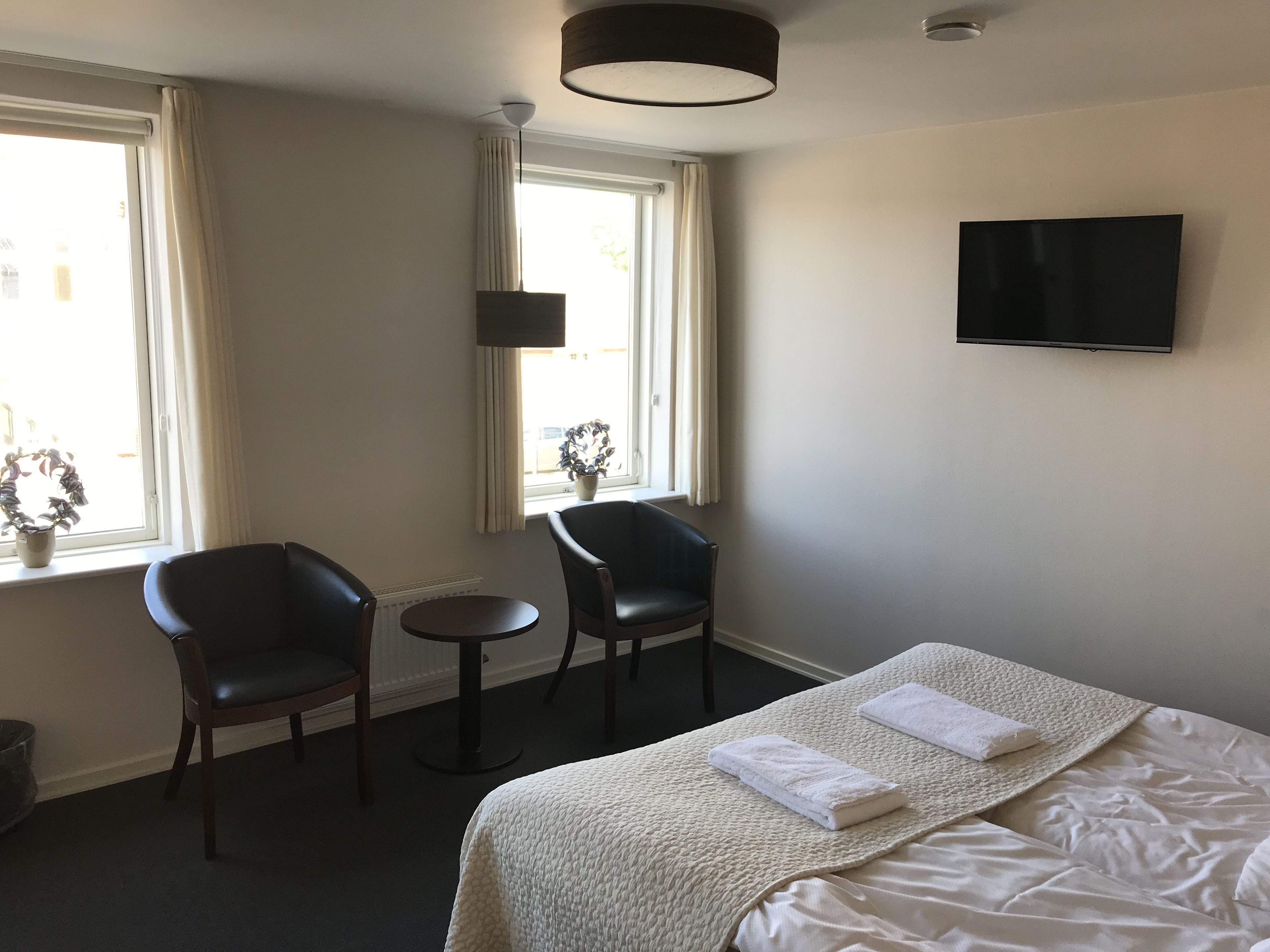 A hotel room with a bed, two chairs, a small table, a TV, and a window with curtains.