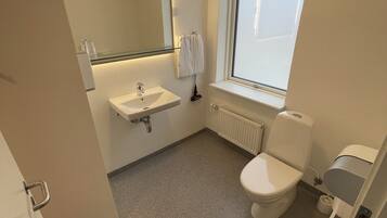 A small, modern bathroom with a white sink, mirror, and toilet. There is a window providing natural light and a towel rack with two towels.