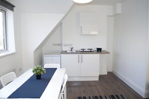 A compact kitchen with white cabinets, a sink, and a small countertop. There is a dining table with chairs and a potted plant.