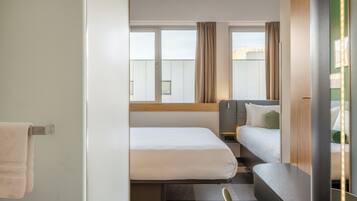 Habitación de hotel con dos camas, una ventana con cortinas, una mesita y un espejo con luces.