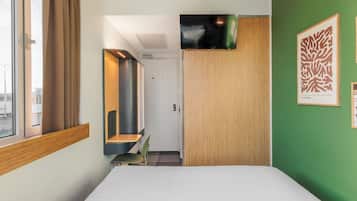 A hotel room with a bed, a desk, a chair, a TV, and artwork on the wall.