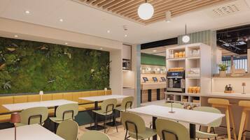 Un café moderno con sillas verdes, techo de madera y pared verde con plantas.