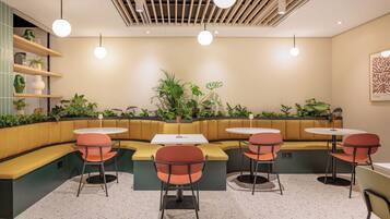 Un intérieur moderne avec des tables rondes et des chaises orange, un mur végétal, et un plafond orné de lambris en bois et de luminaires suspendus.