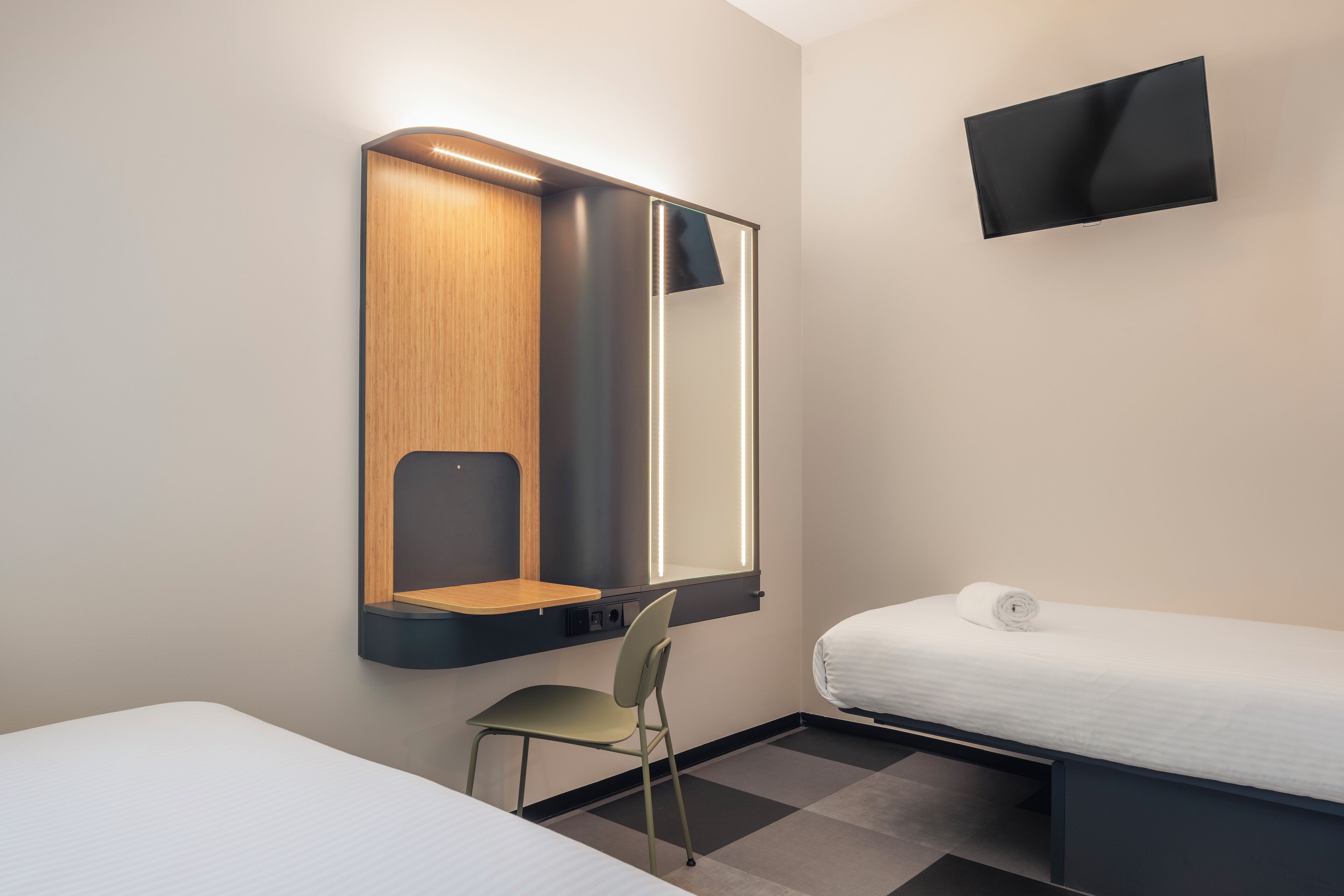 Una camera d'albergo con un letto, una sedia, una scrivania con uno specchio e una TV a schermo piatto montata a parete.
