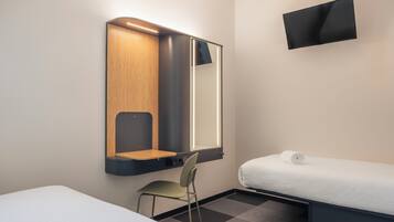 Una camera d'albergo con un letto, una sedia, una scrivania con uno specchio e una TV a schermo piatto montata a parete.