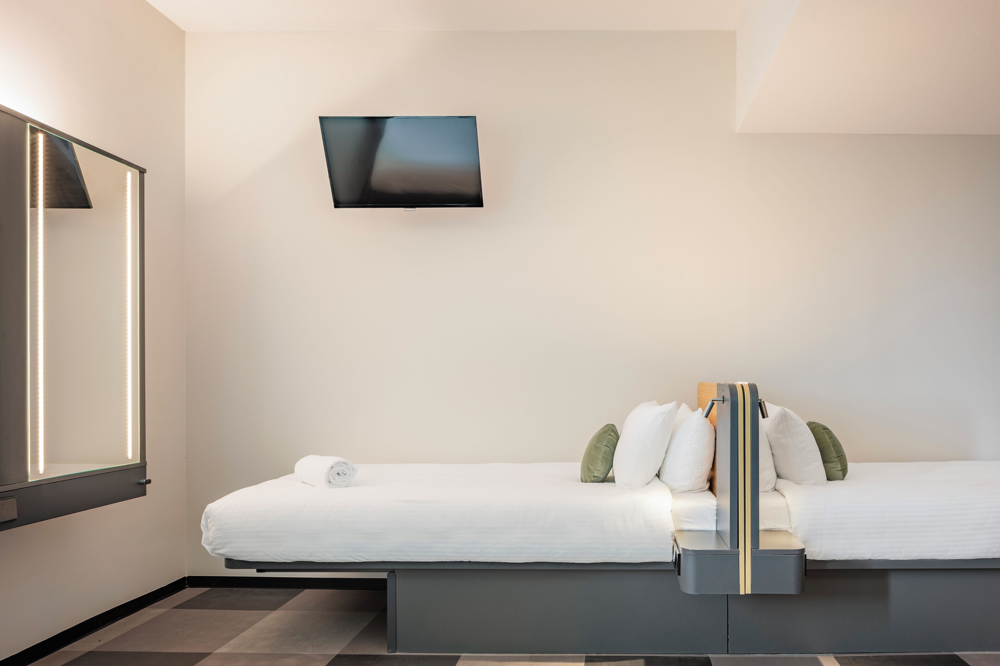 Ein modernes Hotelzimmer mit Bett, Flachbildfernseher an der Wand und integriertem Nachttisch.