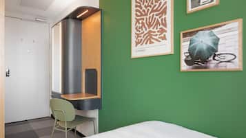 Una habitación de hotel con una cama, un escritorio con silla, pared verde y obras de arte.
